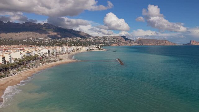 Albir and Altea Costa Blanca Spain.Distant slow reveal of golden sandy beach over crystal clear blue sea with views of Peacock Island, the mountains and interesting clouds in bright sun