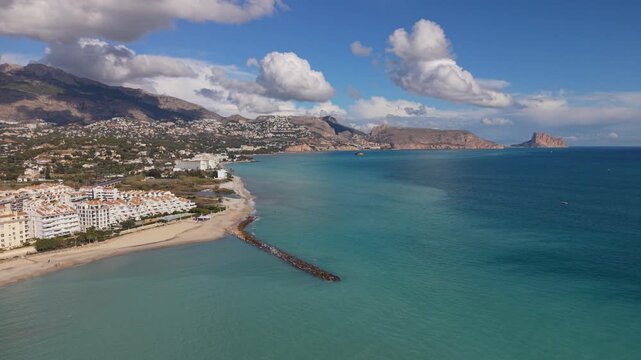 Albir and Altea Costa Blanca Spain.Drone flying over crystal clear blue sea and beach towards the headland and Peacock Island with mountains and interesting clouds in bright sunshine