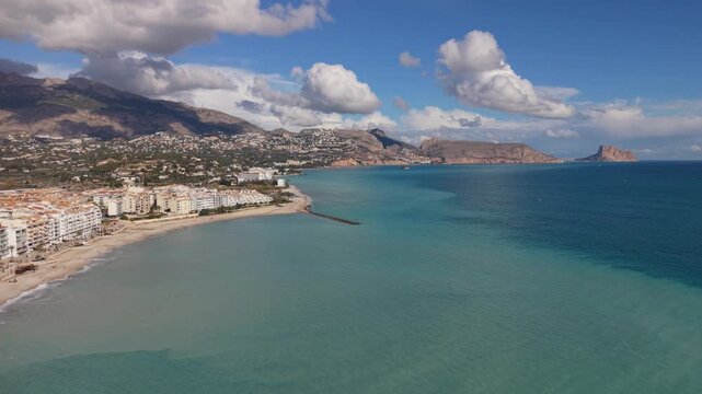 Albir and Altea Costa Blanca Spain.Drone flying over crystal clear blue sea and beach towards the headland dividing the resorts from Benidorm with mountains and interesting clouds in bright sunshine