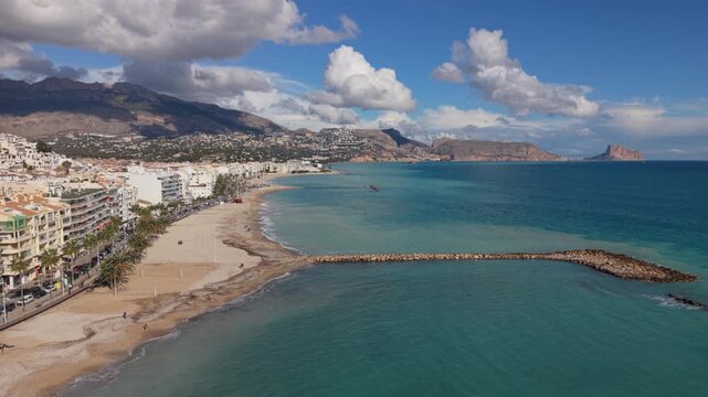 Albir and Altea Costa Blanca Spain.Reveal over the breakwater of golden sandy beach, crystal clear blue sea with views of Peacock Island, the mountains and interesting clouds in bright sun