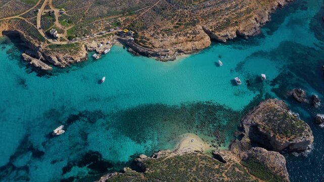 Crystal-clear Turquoise Waters Embrace the Rugged Shores and Hidden Coves of the Blue Lagoon on Comino Island, Malta - Orbit Drone Shot