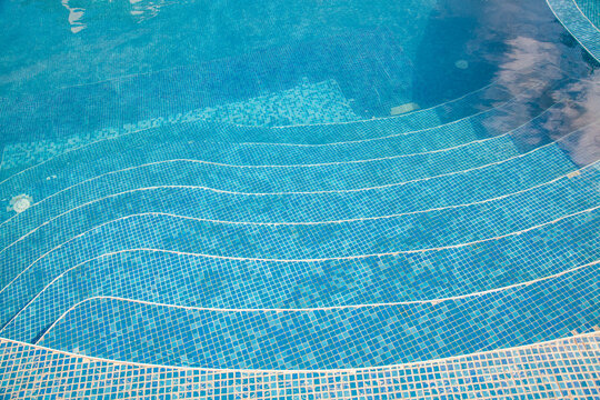 Crystal clear blue swimming pool with steps, luxury resort hotel pool detail, summer vacation background