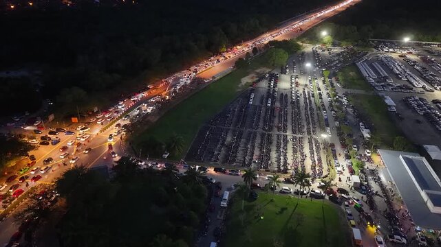Night aerial of Batu Kawan Modifighter festival showing parked motorcycles and heavy vehicle traffic.