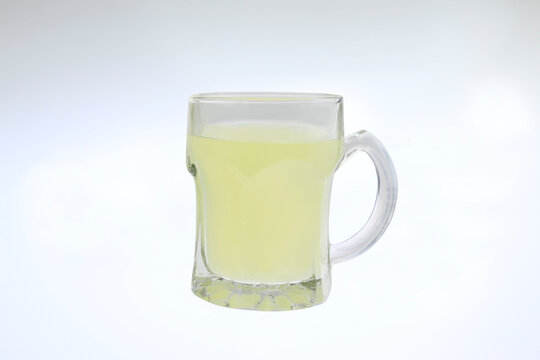 Fresh infused water in a transparent glass mug isolated on white background. Glass mug holds pale yellow liquid.  healthy detox water, vitamin C infused drink, cold refreshing natural immune booster. 