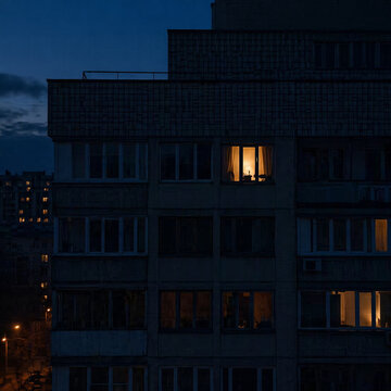 AI generated dark apartment facade at night with single warm lit window creating contrast solitude urban life and quiet atmosphere with copy space
