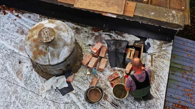 Worker performing bricklaying tasks on a rooftop, preparing mortar and building chimney