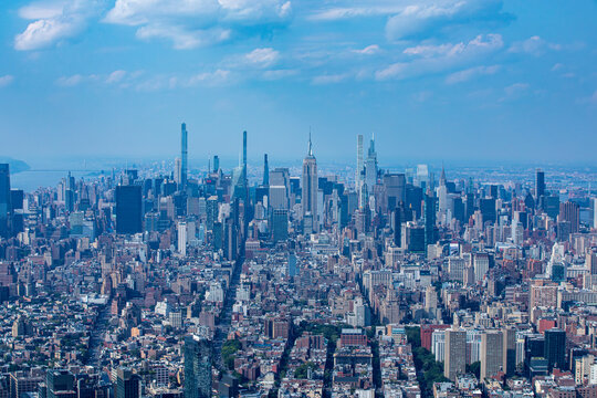 Aerial view of the Empire State Building and Midtown Manhattan skyscrapers under a bright blue sky in New York, New York, United States.