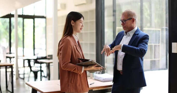 Two business people partners coworkers colleagues discussing about work at office stairs. Female workers manager showing document contract graphs and charts for her mature senior boss