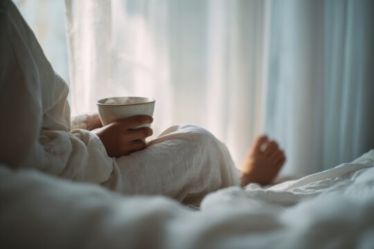 faceless woman with tea cup resting on soft bed linen in warm daylight, cozy bedroom atmosphere and relaxed moment, therapeutic laziness, lifestyle comfort relaxation