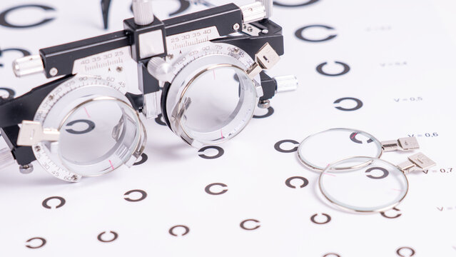 Phoropter lies beside an eye chart. Its two large lenses point toward the letter symbols. Black 'C' and 'O' shapes cover the white surface. Ideal for eye examination or vision testing scenarios