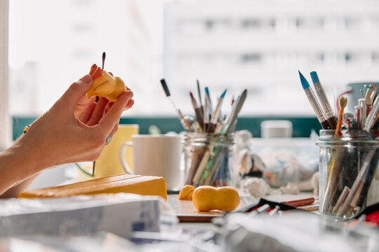 Hands of an artist sculpting yellow clay with tools in a bright creative studio