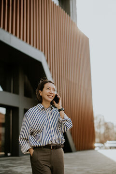 Korean woman talking on the phone outside a modern building on a sunny day