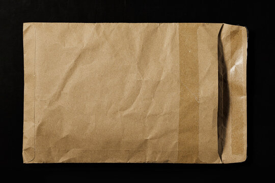 A textured brown kraft paper mailer envelope with wrinkles isolated on a dark black background. Blank mockup for packaging.
