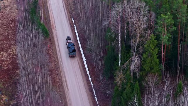 Tractor with trailer hauling hay bales along an unpaved road through a forest area