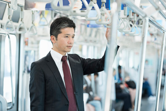 電車内でスマートフォンを操作する40代男性ビジネスマン