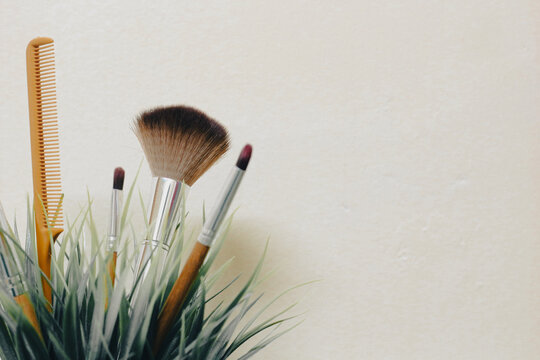 Makeup Brushes and Hair Comb with Green Plant on Beige Background, Beauty and Cosmetics Flat Lay