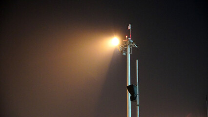 Obraz premium High mast airport lighting pole against dark misty night sky illumination for aviation ground operations and terminal safety security transportation infrastructure background