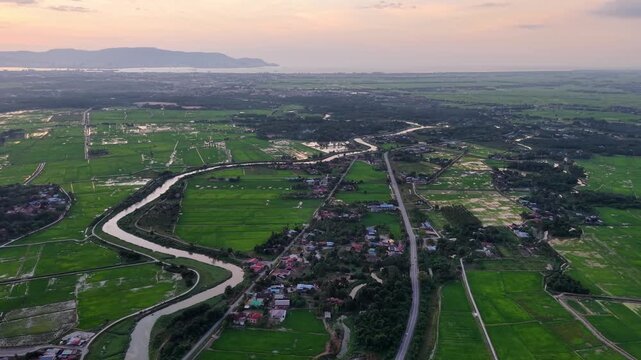 Aerial drone view of Kubang Semang village, river and surrounding rice paddies at sunset.