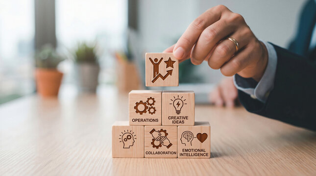 Hand places top success block on wooden pyramid with text: operations, creative ideas, collaboration, emotional intelligence, business growth