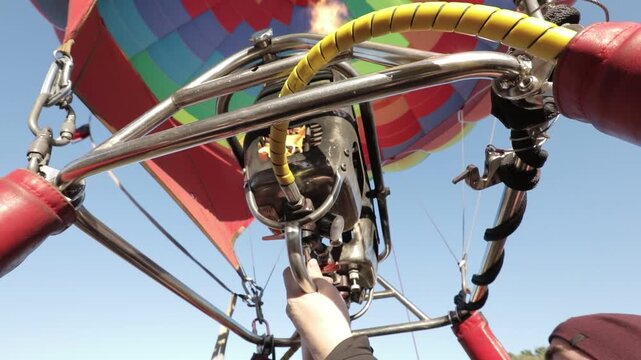 A vibrant hot air balloon with a colorful pattern is being inflated under a clear blue sky, viewed from the basket.