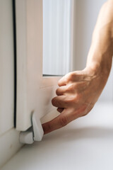 Naklejka premium Vertical close-up shot of hand operating white latch on modern pvc window. Natural light illuminates scene, focusing on home safety, security, and maintenance. Minimalist and clean composition.