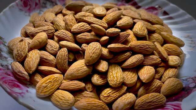 Raw almond nuts on a floral ceramic plate, heap of organic brown almonds, healthy vegan snack and protein rich superfood ingredients
