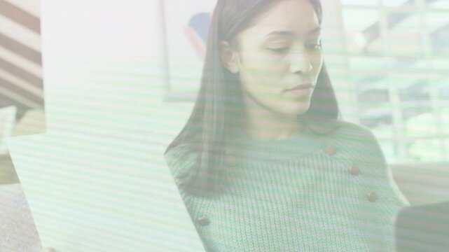 Woman sitting on couch reviewing printed page, shifting gaze to laptop and entering business data