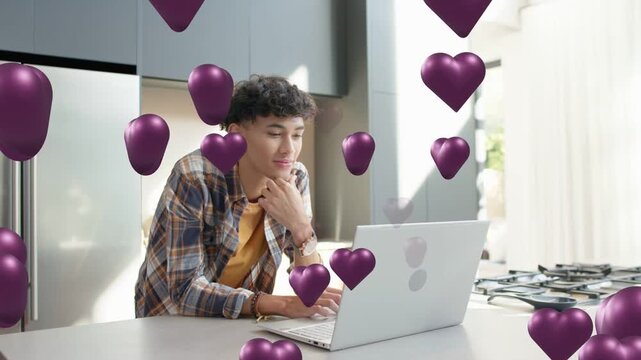 Man sitting in kitchen, laptop receiving social message, purple hearts filling frame around him