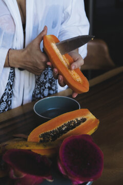 Person cutting papaya with dragon fruit on wooden table, Bali