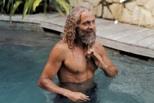 Happy mature man with long curly hair rising from pool, Bali