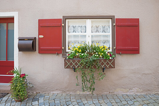 rough facade and window with red shutters. flowerbox with spring flowers