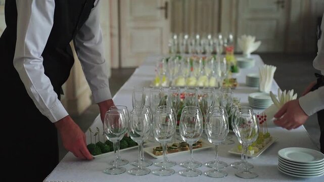 Elegant table setup. Preparing for sophisticated celebration. Arranging fine glassware and delicacies for refined event. Carefully organizing crystal stemware and hors d oeuvres for formal gathering