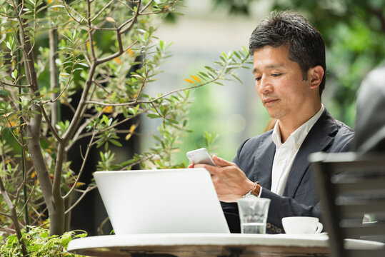 カフェテラスでスマートフォンを確認する40代男性
