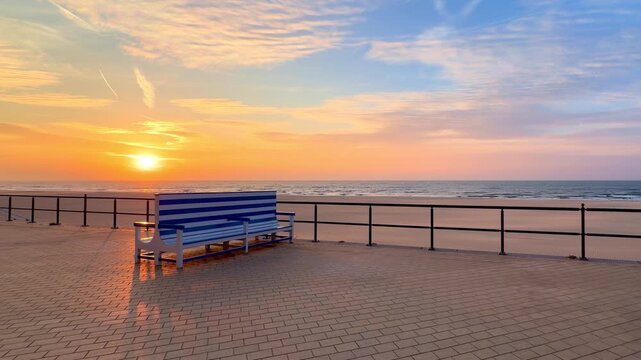 Empty Blue Striped Bench on a Seaside Promenade Overlooking a Tranquil Ocean Sunset