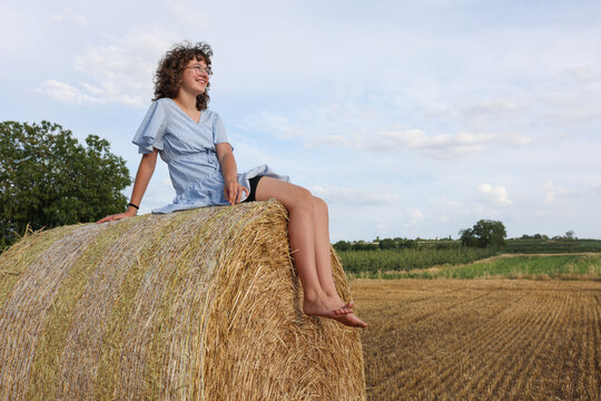 Child sitting barefoot on a hay bale in a summer field