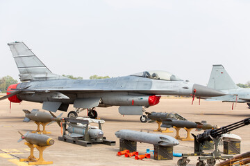 Obraz premium A powerful military fighter jet is displayed on the runway surrounded by a heavy arsenal of bombs, missiles, and ammunition.