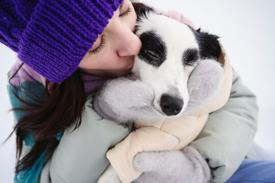 Woman in winter clothing hugging and kissing dog outdoors in snow