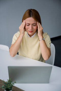 Tired businesswoman sitting at office desk stressed with headache
