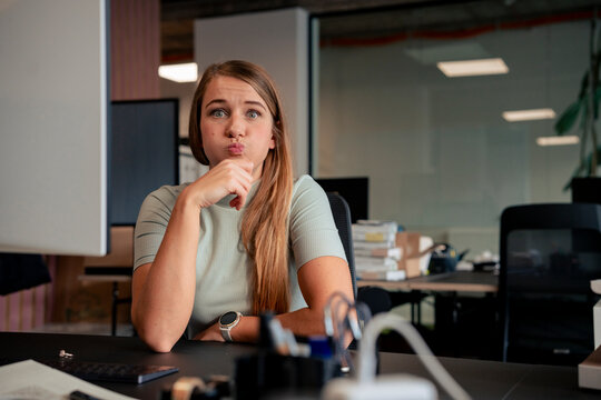 Playful businesswoman with puffed cheeks sitting at desk in office