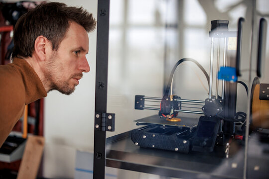 Engineer looking at 3d printer machine inside glass box at workshop