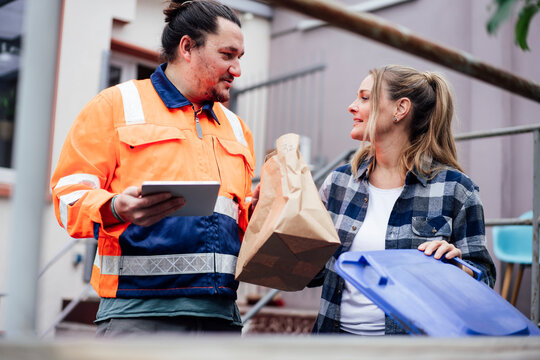 Sanitation worker and woman discussing by garbage bins