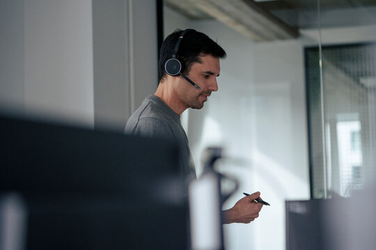 Mature businessman wearing headset and holding pen in office