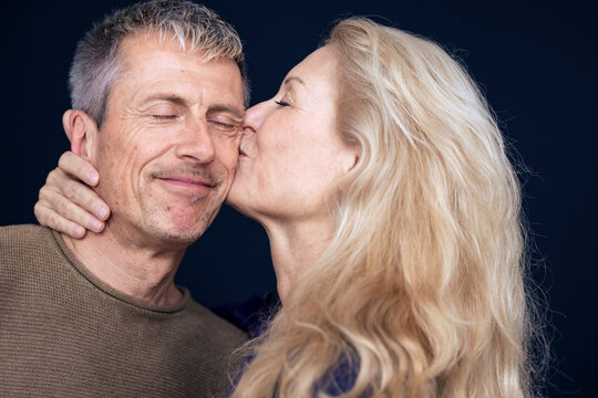 Blond woman kissing man on cheek against black background