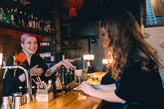 Smiling bartender serving cocktail to customer at bar counter