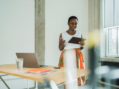 Businesswoman using tablet PC standing near desk at office