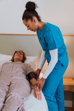 Nurse checking blood pressure of patient in home care bedroom