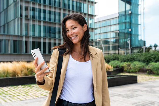 Manager smiling and using smartphone outdoors in financial district