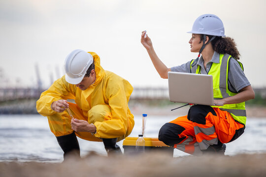 Environmental researchers collecting and examining water samples in test tubes on the coast, Two scientists testing water quality for pollution monitoring using laptop and laboratory equipment