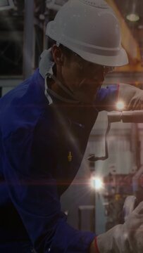 Vertical video: Tech inspecting, turning crank, aligning machine with light flares sweeping factory