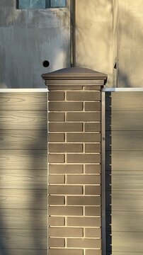 Sunlit brick column by cottage fence, warm golden hour light casts long tree shadows across weathered wooden panels, capstone